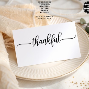 May include: A white rectangular card featuring the black script word thankful centered on the surface. The card includes text listing five file names: thankful, grateful, gather, family, blessed, and a file size of approximately 3 inches H x 11.8 inches W.