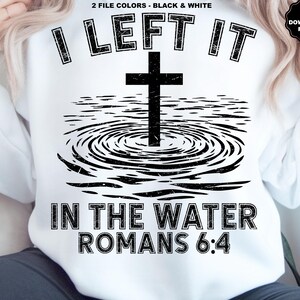 May include: White sweatshirt with a black graphic design. The design features a cross in water with the text "I LEFT IT IN THE WATER ROMANS 6:4". The design is in a distressed style.