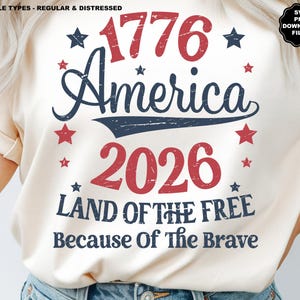 Op de afbeelding: Crèmekleurig T-shirt met een patriottisch ontwerp. Het ontwerp toont de tekst "1776 America 2026 Land of the Free Because of the Brave" in rood en marineblauw, met steraccenten. Het shirt heeft een normale pasvorm.