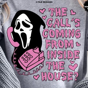 Puede incluir: Una camiseta gris con un gr&aacute;fico de una m&aacute;scara de Ghostface sosteniendo un tel&eacute;fono rosa. El texto "THE CALL'S COMING FROM INSIDE THE HOUSE?" est&aacute; en rosa, con corazones. Incluye archivos de descarga SVG y PNG.