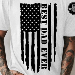 K&ouml;nnte beinhalten: Ein wei&szlig;es T-Shirt mit einem schwarz-wei&szlig;en amerikanischen Flaggen-Design. Der Text "BEST DAD EVER" ist vertikal auf der Flagge gedruckt.