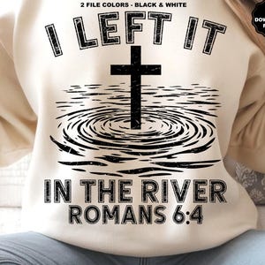 Pu&ograve; includere: Felpa color crema con grafica nera. La grafica presenta una croce sopra increspature d'acqua, con il testo "I LEFT IT IN THE RIVER ROMANS 6:4". Il design &egrave; invecchiato, conferendogli un aspetto vintage. L'angolo in alto a destra ha un logo "SVG PNG DOWNLOAD FILES".
