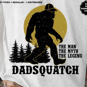 Può includere: Una maglietta bianca con una silhouette nera di Bigfoot che indossa un berretto da baseball. La silhouette è davanti a un sole giallo e una foresta. Il testo "The Man The Myth The Legend" è sotto la silhouette e il testo "DADSQUATCH" è in fondo alla maglietta.