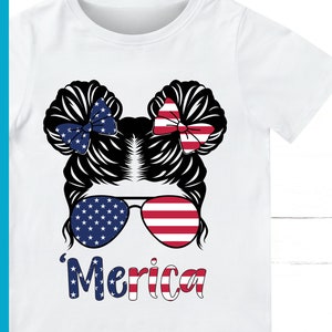 May include: A white t-shirt featuring a black and white illustration of a girl with her hair in two buns. The girl is wearing sunglasses with an American flag design. The text "Merica" is below the illustration.