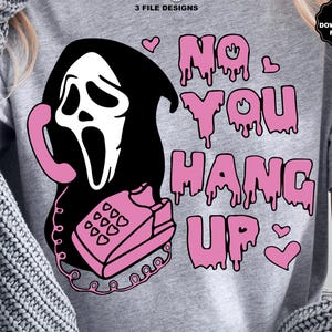 Puede incluir: Camiseta gris con un gr&aacute;fico de una m&aacute;scara de Ghostface sosteniendo un tel&eacute;fono rosa. El texto "NO YOU HANG UP" est&aacute; en letras rosas goteando, con corazones rosas. El dise&ntilde;o tiene un tema espeluznante de Halloween.