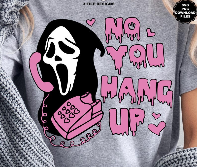 Puede incluir: Camiseta gris con un gr&aacute;fico de una m&aacute;scara de Ghostface sosteniendo un tel&eacute;fono rosa. El texto "NO YOU HANG UP" est&aacute; en letras rosas goteando, con corazones rosas. El dise&ntilde;o tiene un tema espeluznante de Halloween.