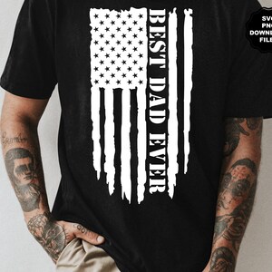K&ouml;nnte beinhalten: Ein schwarzes T-Shirt mit einem wei&szlig;en, abgenutzten amerikanischen Flaggen-Design und dem Text "BEST DAD EVER", der vertikal auf der Flagge gedruckt ist.