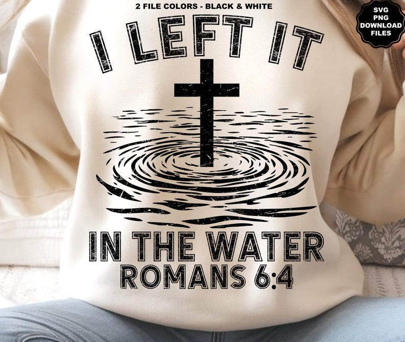 May include: Cream-colored sweatshirt with a black graphic design. The design features a cross above water ripples, with the text "I LEFT IT IN THE WATER ROMANS 6:4". The sweatshirt has a crew neck and long sleeves.