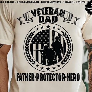 May include: A white t-shirt with a black graphic design featuring a silhouette of two soldiers standing in front of an American flag. The text "Veteran Dad" is above the image and "Father-Protector-Hero" is below the image.