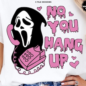 Puede incluir: Camiseta blanca con un gr&aacute;fico rosa y negro de un personaje de cara de fantasma sosteniendo un tel&eacute;fono rosa. El texto "NO YOU HANG UP" est&aacute; en letras rosas goteando, con corazones rosas. El dise&ntilde;o es una descarga digital.