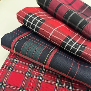 May include: Three folded pieces of fabric featuring distinct tartan patterns. The top piece is dark red and black, the middle piece is navy blue with green and yellow lines, and the bottom piece is bright red with green, white, and yellow lines.