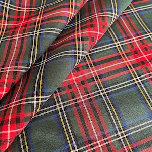 May include: Close-up of a folded fabric with a traditional tartan pattern. The fabric has a dark green base, overlaid with red, white, yellow, and blue lines. The design creates a classic plaid, suitable for clothing or home decor. The fabric is likely cotton.