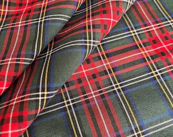 Puede incluir: Primer plano de una tela doblada con un patrón de cuadros clásico. La tela presenta un fondo verde oscuro con líneas rojas, blancas, amarillas y azules que se cruzan, creando un diseño tartán tradicional. La tela es probablemente de algodón.