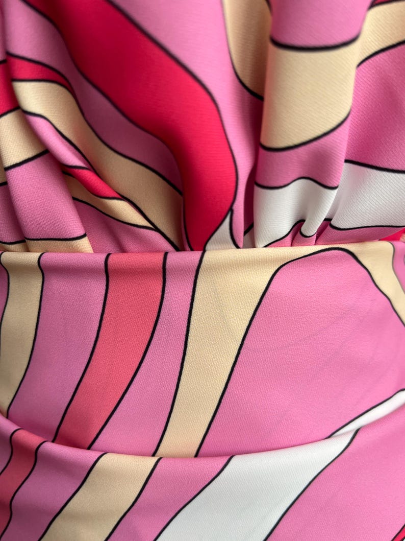 Puede incluir: Primer plano de una tela con un patr&oacute;n vibrante de inspiraci&oacute;n retro. El dise&ntilde;o presenta l&iacute;neas curvas y fluidas en tonos de rosa, rojo, blanco y beige, delineadas en negro. La tela est&aacute; fruncida, creando pliegues y sombras suaves.