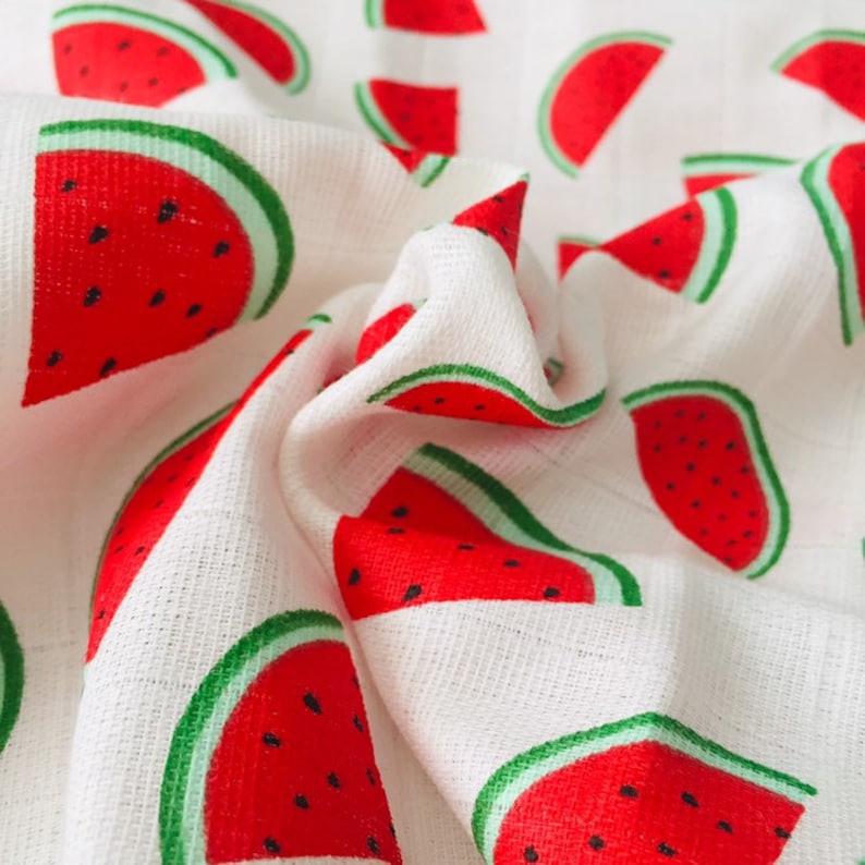 May include: White fabric with a repeating pattern of red watermelon slices. The watermelon slices have green rinds and black seeds.