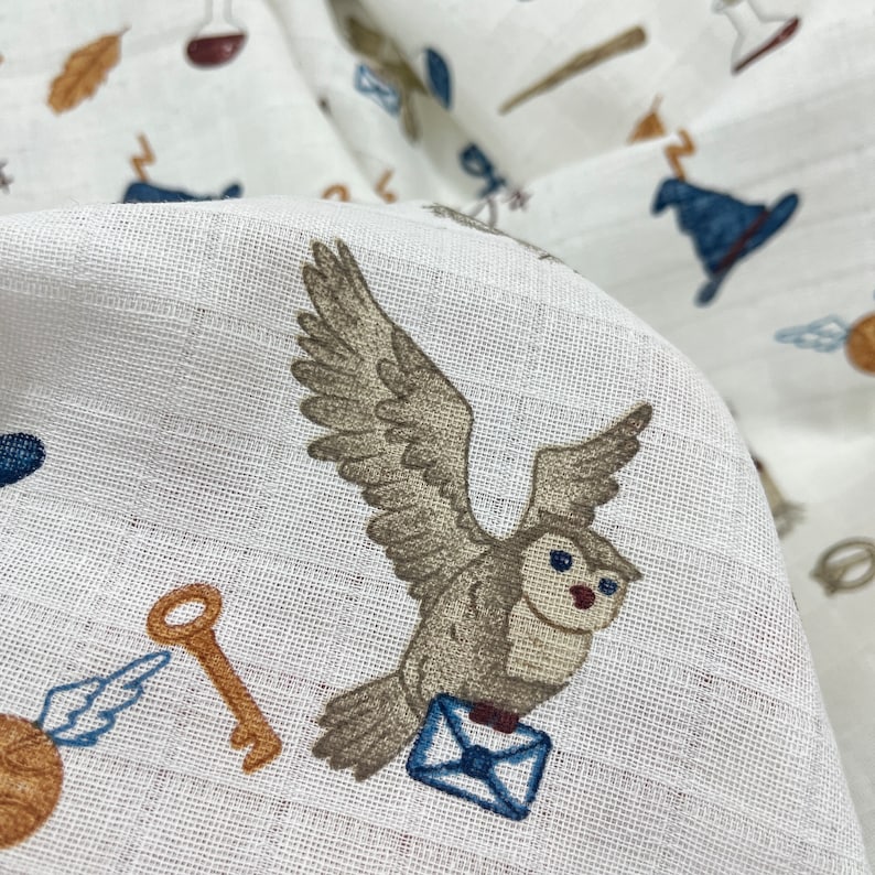 May include: White fabric with a brown owl carrying a blue envelope. The owl is flying with its wings spread. The fabric also has other small images of keys, wands, and other magical objects.