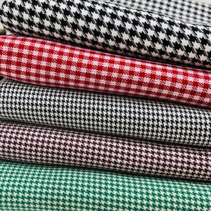 May include: A stack of five fabric swatches in different patterns. The top swatch is black and white houndstooth, followed by red and white gingham, then black and white houndstooth again, then burgundy and white houndstooth, and finally green and white houndstooth.