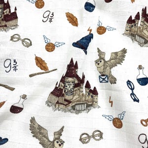 White fabric with a repeating pattern of brown and white owls, brown and white castles, brown and gold wands, brown and gold glasses, brown and gold leaves, brown and gold snitches, and brown and gold 9 3/4 signs.