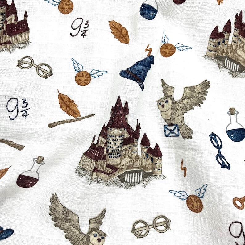 White fabric with a repeating pattern of brown and white owls, brown and white castles, brown and gold wands, brown and gold glasses, brown and gold leaves, brown and gold snitches, and brown and gold 9 3/4 signs.