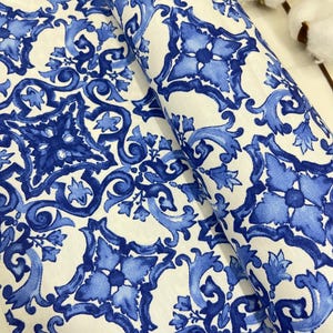 May include: White fabric with a blue and white repeating pattern of stylized floral designs. The fabric is folded in half.