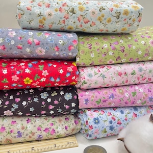 May include: A stack of eight fabric swatches with different floral patterns. The fabrics are in various colors, including blue, gray, red, green, pink, brown, beige, and light blue. The swatches are arranged in a stack, with the top swatch being light blue and the bottom swatch being beige.
