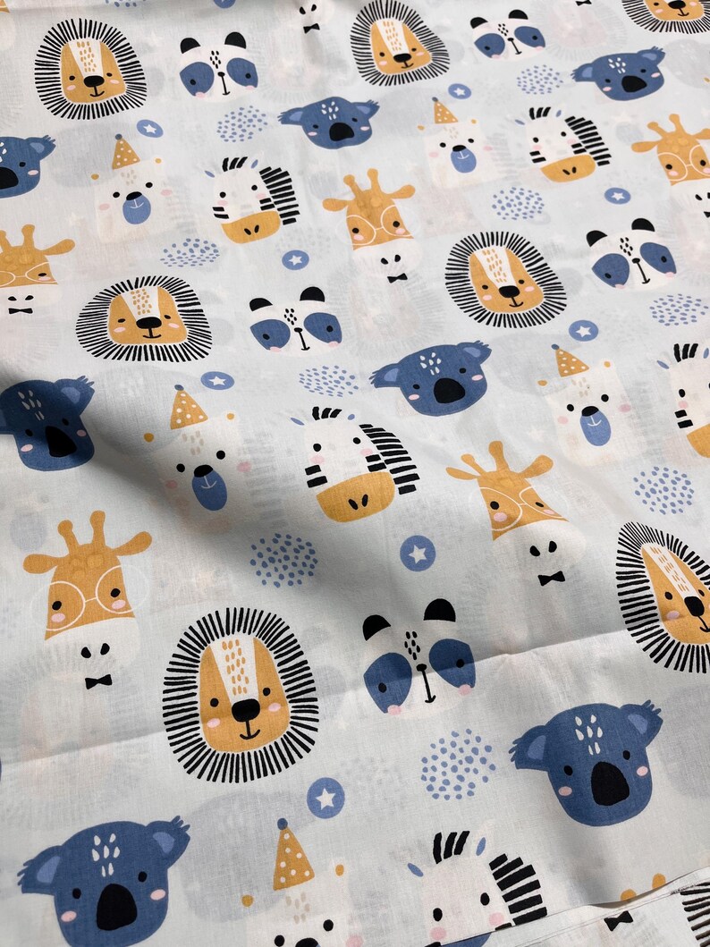 May include: A light blue fabric featuring a repeating pattern of cartoon animal faces including lions with black manes, blue koalas, giraffes with glasses, zebras, and white bears wearing yellow party hats, interspersed with small blue stars and dots.