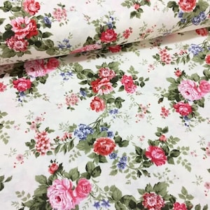 May include: A white fabric with a floral pattern featuring pink, red, and blue roses. The fabric is covered in a repeating pattern of flowers and leaves.