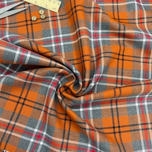 Könnte beinhalten: Orangefarbener, grauer und weißer karierter Stoff mit gewebter Struktur. Der Stoff ist gefaltet und drapiert.