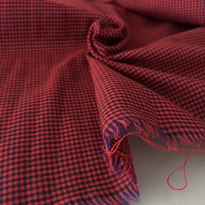 May include: Red and black gingham fabric with a frayed edge. The fabric is folded and has a textured surface.