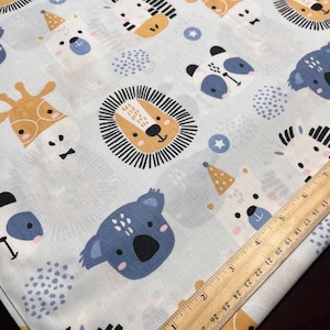 May include: A light blue fabric featuring a repeating pattern of cartoon animals including lions, koalas, pandas, giraffes, and zebras, alongside small stars and dots. A wooden ruler is placed diagonally, showing measurements in inches.