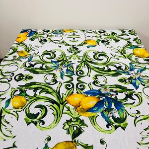 Puede incluir: Mantel rectangular blanco con un dise&ntilde;o de limones y follaje. El patr&oacute;n presenta limones amarillos, hojas verdes y detalles azules. Adecuado para una mesa de comedor.