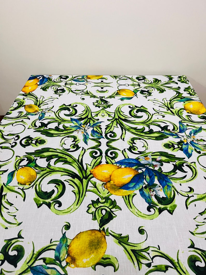 Puede incluir: Mantel rectangular blanco con un dise&ntilde;o de limones y follaje. El patr&oacute;n presenta limones amarillos, hojas verdes y detalles azules. Adecuado para una mesa de comedor.