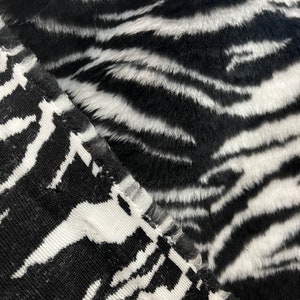 May include: Close-up of two black and white zebra print fabrics. One fabric has a fuzzy texture, while the other has a woven texture.