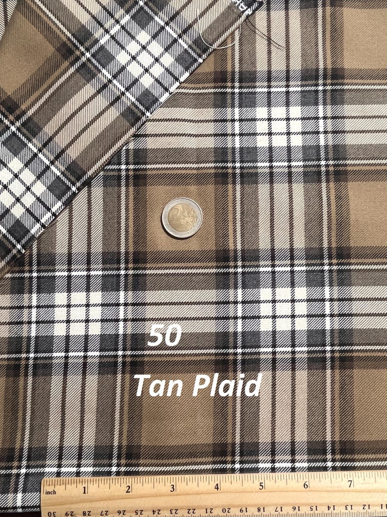 May include: A tan plaid fabric featuring a pattern of intersecting dark brown and white lines. A two-euro coin is placed on the fabric for scale, and a wooden ruler at the bottom shows measurements in inches, with the fabric width spanning seven inches.