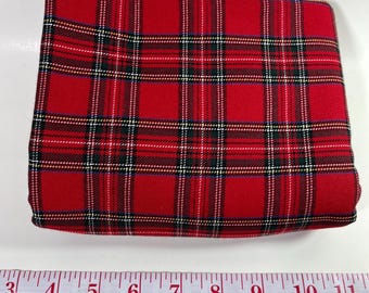 May include: A folded piece of red fabric featuring a classic tartan plaid pattern with intersecting black, white, and yellow lines. A white measuring tape is positioned below the fabric, showing a length measurement from 3 to 11 inches.