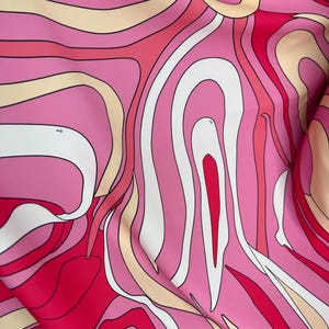 Puede incluir: Primer plano de una tela con un dise&ntilde;o abstracto. El patr&oacute;n presenta l&iacute;neas curvas y fluidas en tonos de rosa, blanco, rojo y beige, creando un efecto psicod&eacute;lico. La tela parece suave, posiblemente seda o sat&eacute;n.