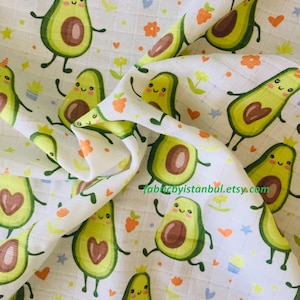 Könnte beinhalten: Weißer Stoff mit einem sich wiederholenden Muster aus grünen Avocados mit braunen Kernen und lächelnden Gesichtern. Die Avocados haben braune Stiele und kleine braune Beine. Der Stoff hat auch kleine orangefarbene Blumen, rote Herzen und blaue Sterne.