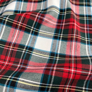 May include: A close-up of a red, white, and green plaid fabric. The fabric has a woven texture and is folded in a way that shows the different colors and patterns.