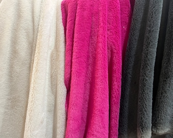 May include: Three pieces of plush fabric hanging vertically side by side. The left piece is cream-coloured, the middle piece is a vibrant hot pink, and the right piece is a dark charcoal grey. Each fabric features a soft, fuzzy, faux fur texture.