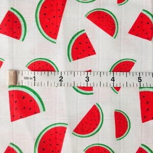 May include: White fabric with a repeating pattern of red watermelon slices. A white measuring tape with black markings is placed on top of the fabric. The tape reads "120 in 1 2 3 4 5".