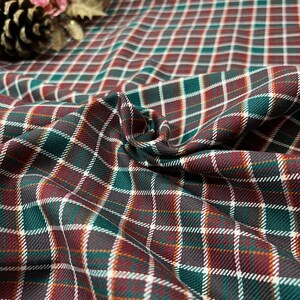 May include: Green, red, and white plaid fabric with a woven texture. The fabric is folded and draped, showing the pattern.