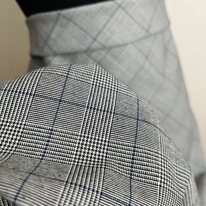 Può includere: Primo piano di un tessuto a quadri grigio e nero con un filo blu sottile che attraversa il motivo.