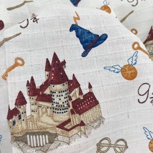 A white fabric with a repeating pattern of  themed images. The images include a castle, a wizard's hat, a golden key, a snitch, and the words '9 3/4'.