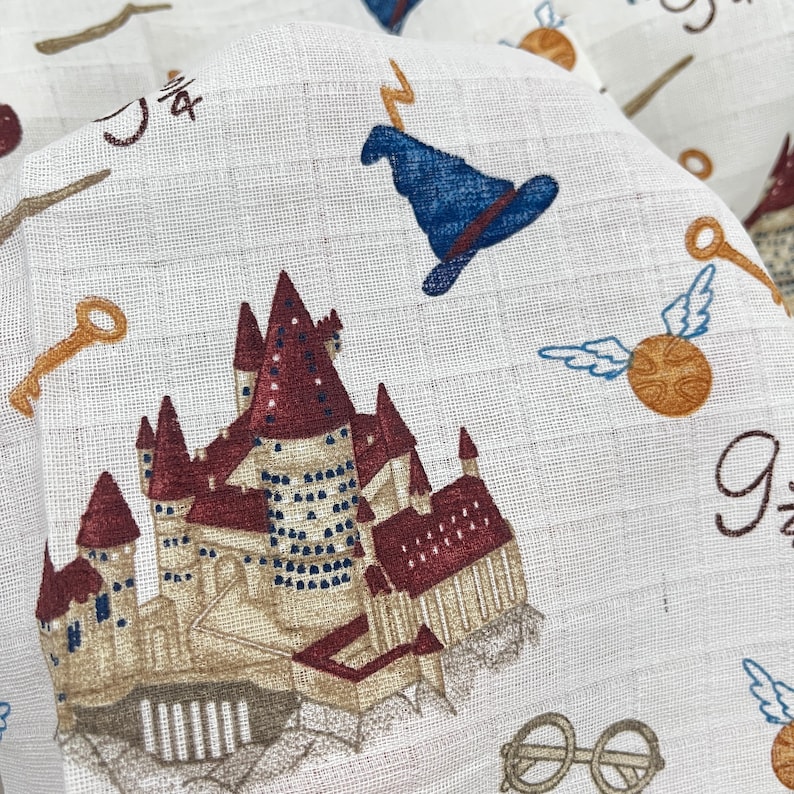 A white fabric with a repeating pattern of  themed images. The images include a castle, a wizard's hat, a golden key, a snitch, and the words '9 3/4'.