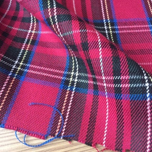 May include: Red, black, white and blue plaid fabric with a woven texture. The fabric is folded and the edges are frayed.