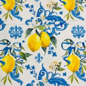 May include: White fabric with a repeating pattern of yellow lemons, blue ribbons, and floral accents. The design includes blue scrollwork and small blue flower clusters, creating a vibrant and decorative print.