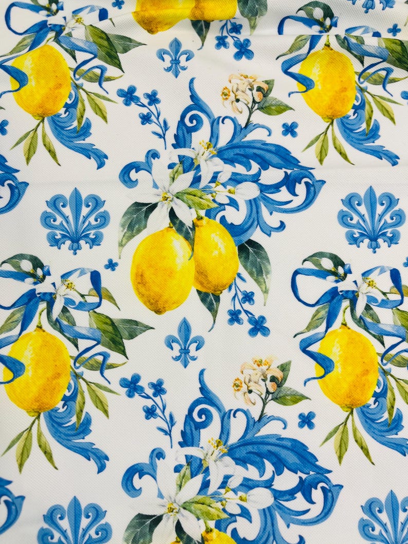 May include: White fabric with a repeating pattern of yellow lemons, blue ribbons, and floral accents. The design includes blue scrollwork and small blue flower clusters, creating a vibrant and decorative print.