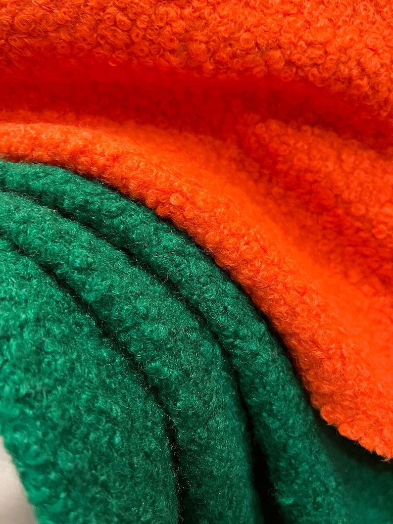 May include: Close-up of two layers of textured fabric. The top layer is a vibrant orange, and the bottom layer is a deep green. The fabric has a soft, fuzzy texture, with visible curls and a slight sheen. The folds of the fabric create shadows and depth.
