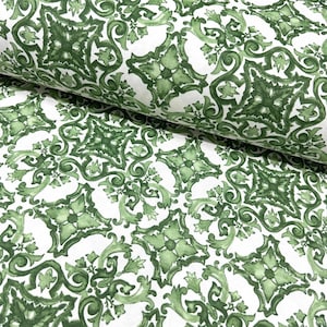 May include: White fabric with a repeating pattern of green floral and geometric shapes. The design features stylized leaves and symmetrical arrangements, creating a classic, decorative look. The fabric is folded, showing the texture and depth of the material.