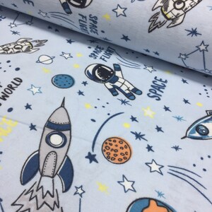 May include: Blue fabric with a space-themed print featuring rockets, astronauts, planets, and stars. The fabric has the words "Space Flight" and "Space" printed on it.